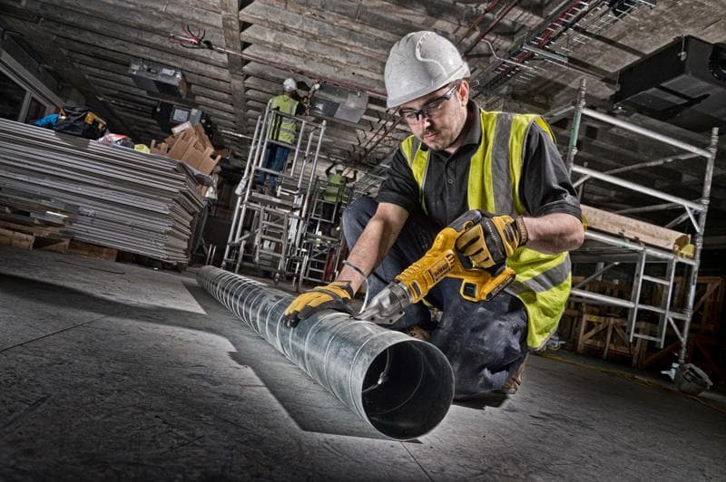 Ouvrier utilise une cisaille sans fil DEWALT sur tuyau. Équipement de sécurité et outils visibles.