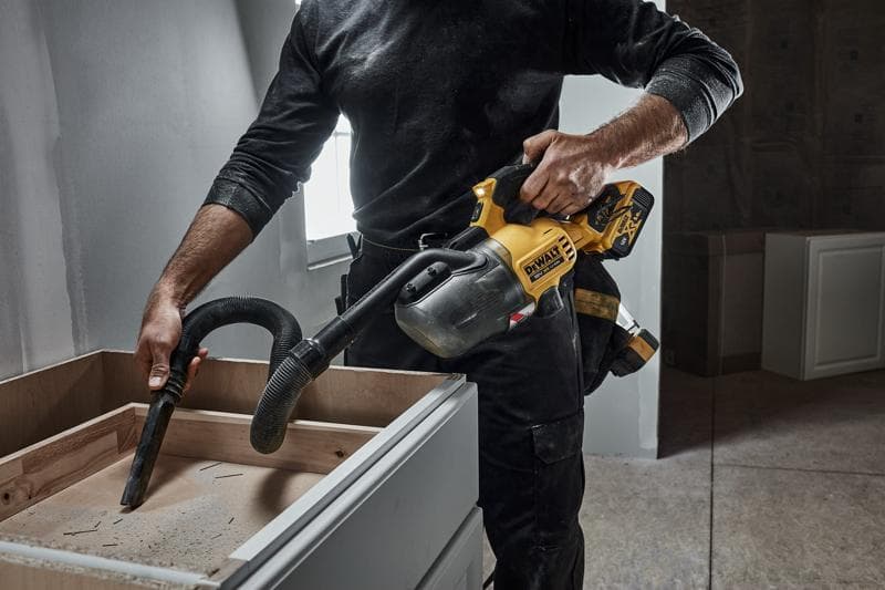 Personne nettoie la poussière d’un meuble en bois avec un aspirateur portatif DEWALT sans fil en chantier.