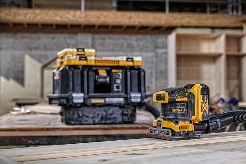 Ponceuse sans fil DEWALT sur bois, boîte de rangement en arrière-plan dans un atelier.